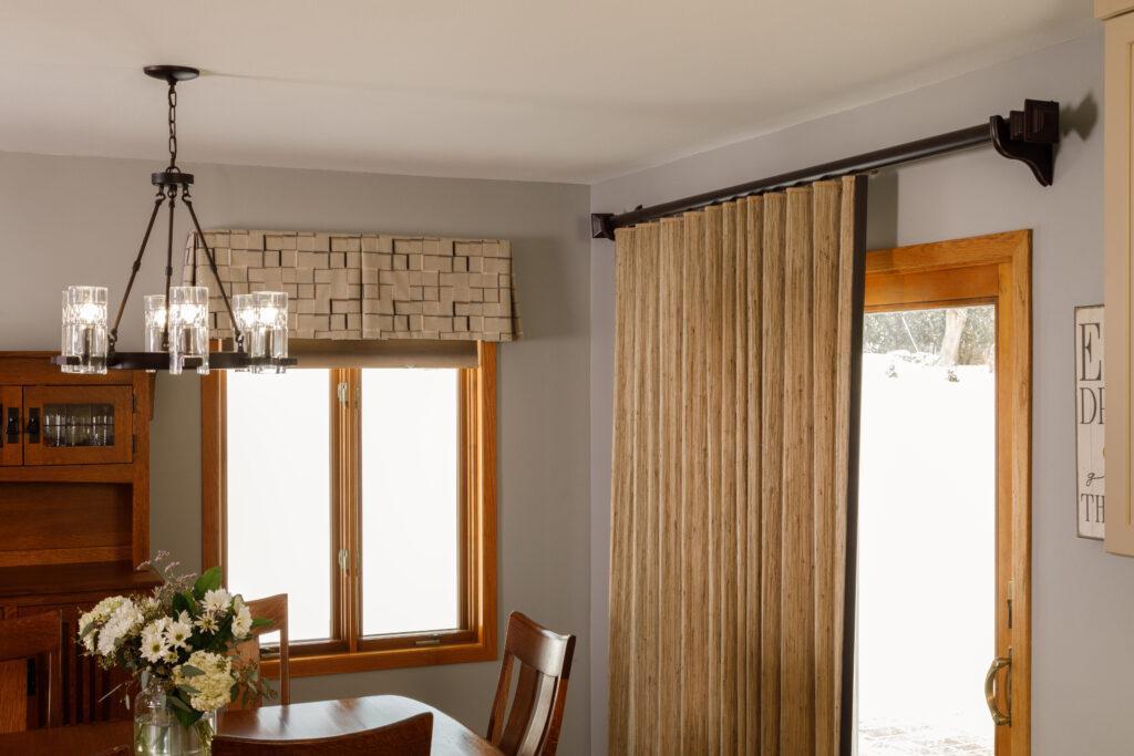 A board mounted valance adds pattern while hiding the cell shade headrail underneath. The patio door features a pole mounted woven wood shade, lined for light and climate control.